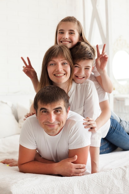 Smiling girl gesturing victory sign on bed with her parent and brother