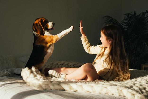 Photo smiling girl giving high-five to dog on bed at home