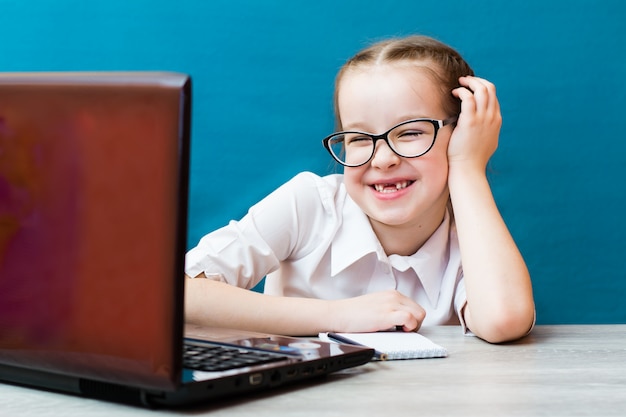 La ragazza sorridente in vetri lavora ad un computer portatile al tavolo