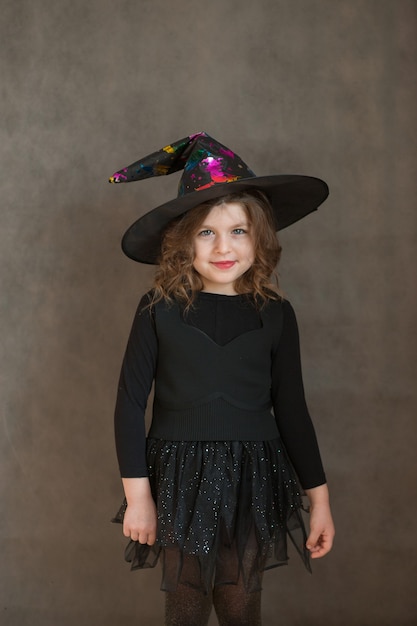 Smiling girl in halloween witch costume on gray background