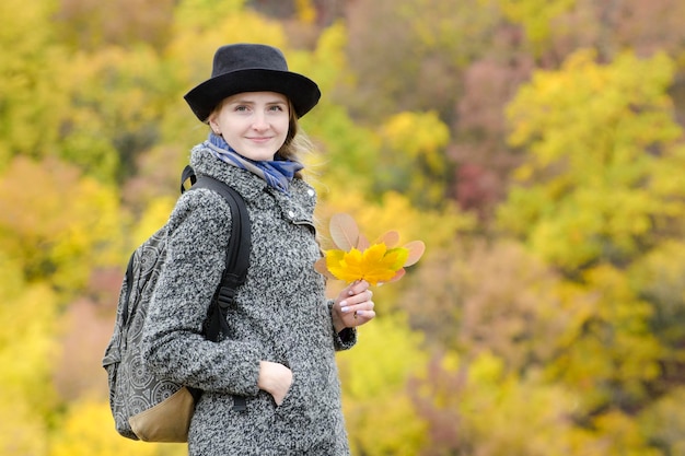 Smiling girl in a hat in autumn park Bright foliage on the background Portrait