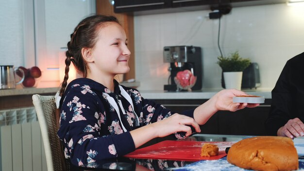 Ragazza sorridente che aiuta sua madre a produrre i biscotti del pan di zenzero