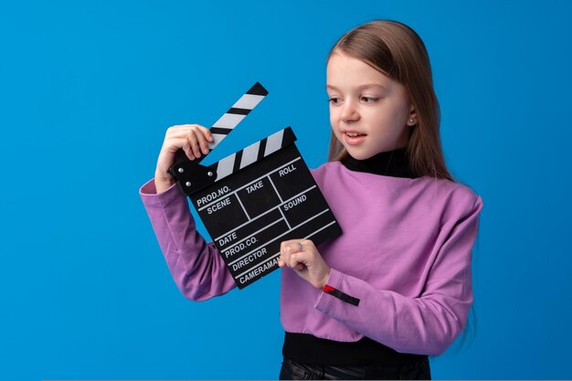 Smiling girl holding clapper board against blue background