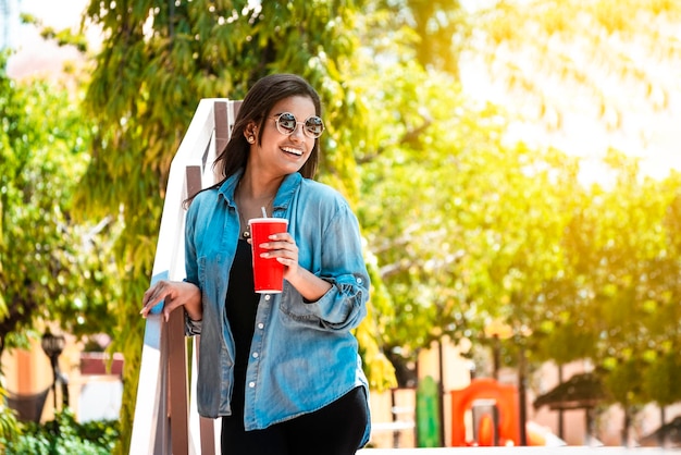 Smiling girl holding a drink on a sunny day A smiling girl holding a drink outside with copy space Portrait of smiling girl in glasses holding drink outdoors