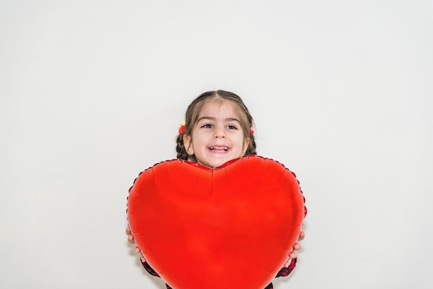 Photo smiling girl holding heart shape balloon while standing against wall