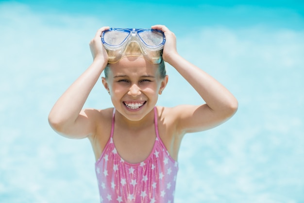 Улыбающаяся девочка держит очки для плавания возле бассейна