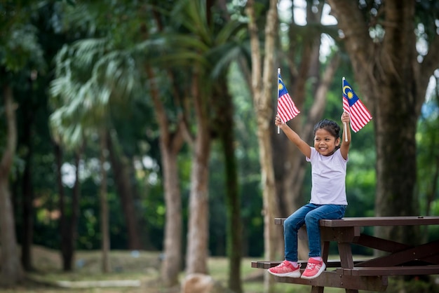 公園のベンチに座ってマレーシアの国旗を掲げている笑顔の少女