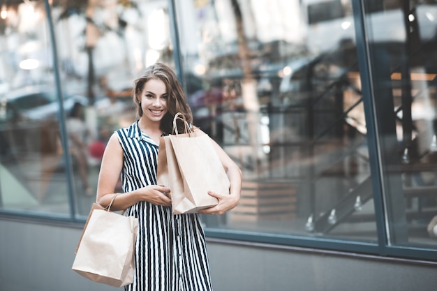 Smiling girl holding paper bags walking over shopwindow