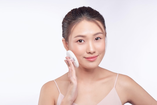 Smiling girl holding powder cushion puff applying cosmetic powder on face