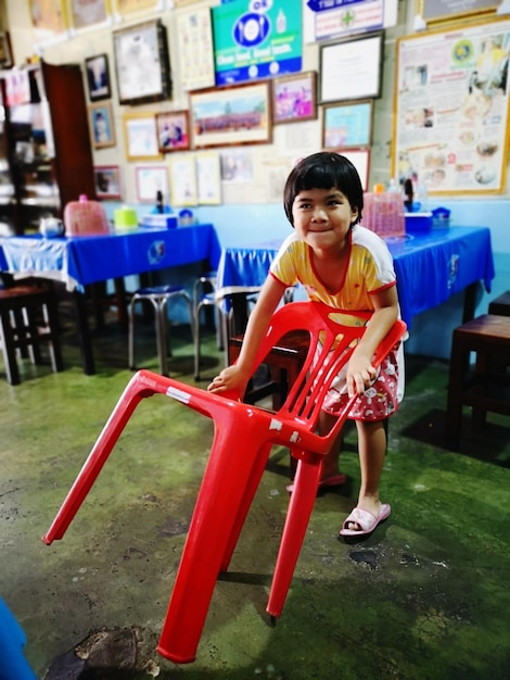 写真 屋内で立っている赤い椅子を握っている笑顔の女の子