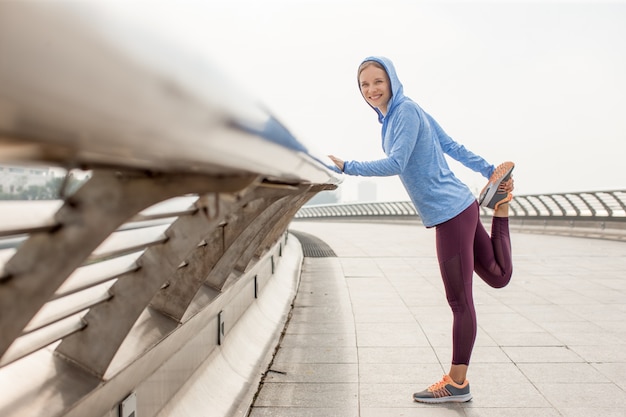 Photo smiling girl holding and stretching leg on bridge