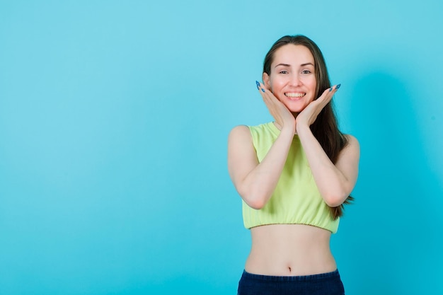 Smiling girl is holding hands under chin on blue background