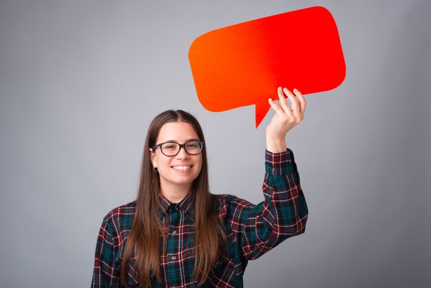 Smiling girl is holding a red bubble speech on grey