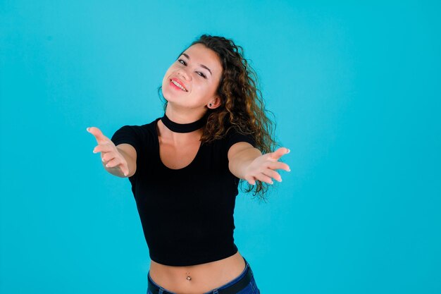 Smiling girl is looking at camera by extending hands to camera on blue background