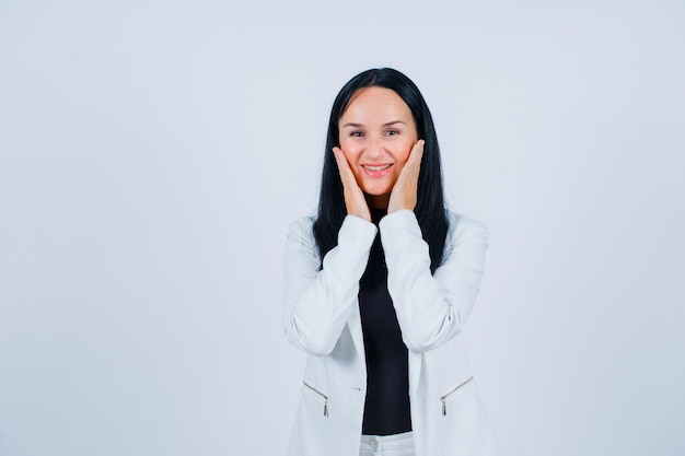 Smiling girl is looking at camera by holding hands on cheeks on white background