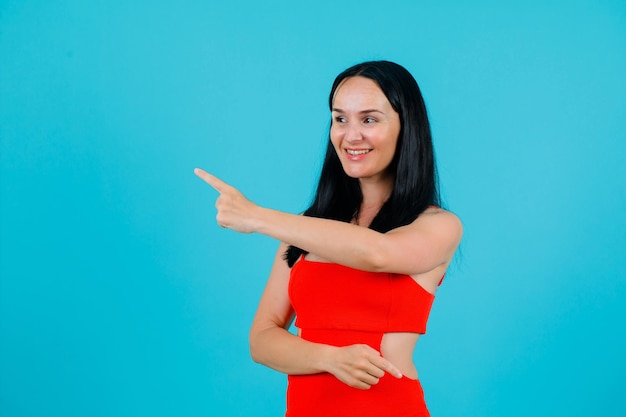 Smiling girl is pointing left with forefinger on blue background