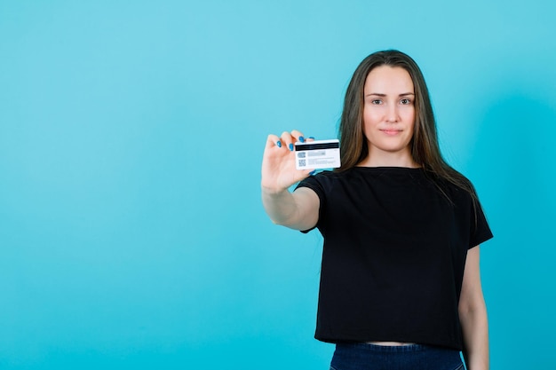 La ragazza sorridente sta mostrando la carta di credito alla fotocamera su sfondo blu