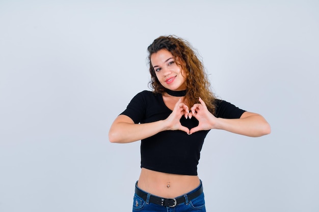 Smiling girl is showing heart gesture on white background