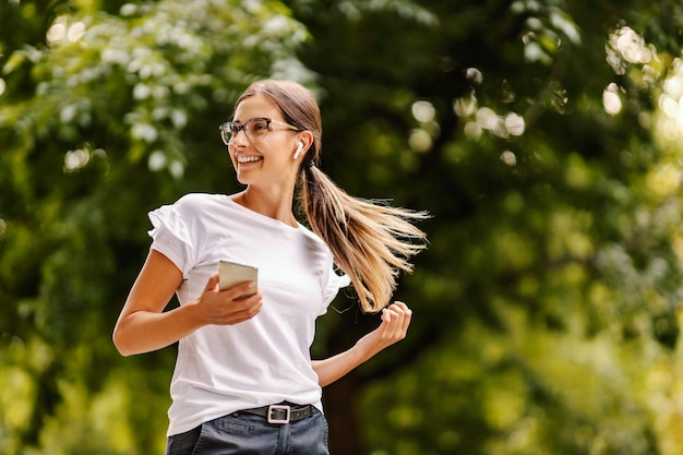 A smiling girl is walking in the park on a beautiful day and listening podcast on the phone