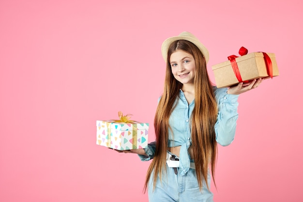 Smiling girl in jeans clothes and straw hat isolated on pink wall.