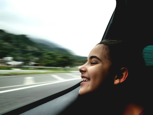 Foto ragazza sorridente che guarda dalla finestra di un'auto sulla strada
