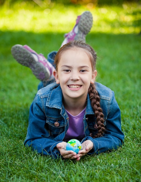 Smiling girl lying on grass and holding Earth in hands