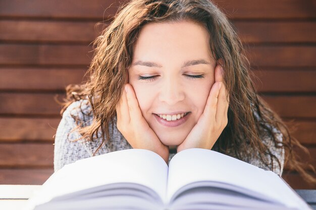 Smiling girl in park with book. Woman reading book on the bench