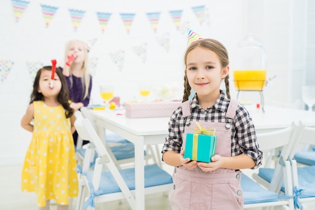 Smiling girl in party hat holding blue gift box