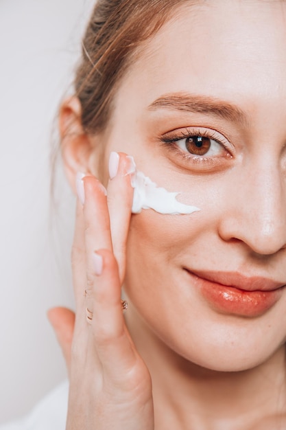 La ragazza sorridente mette la crema sul viso pulito