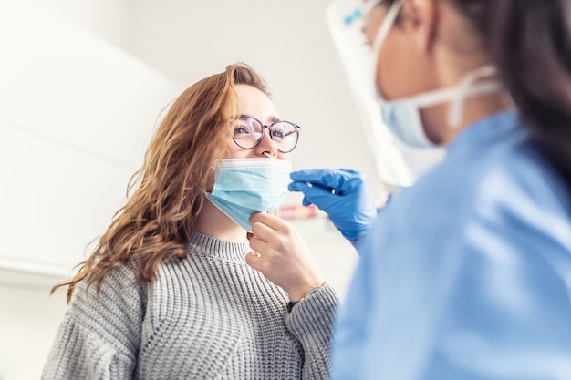 La ragazza sorridente si toglie la maschera dal naso in modo che un operatore sanitario possa prelevare un campione per il test covid-19.