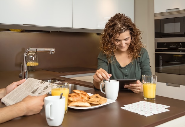 Улыбающаяся девочка читает новости в планшете за завтраком