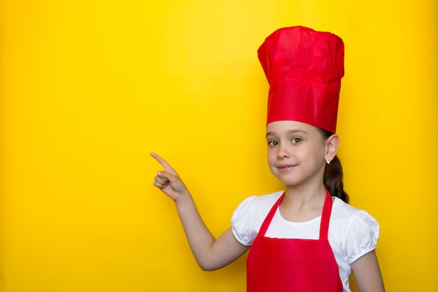 빨간 요리사의 양복에 웃는 소녀는 노란색에 글자를위한 공간에서 그녀의 손가락을 가리 킵니다