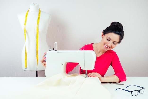Улыбающаяся швея работает на швейной машине и манекене с желтой измерительной лентой на белом фоне