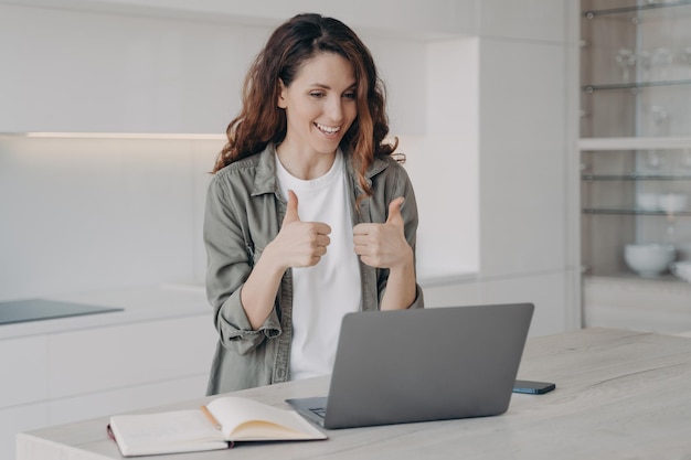 Smiling girl show thumb up gesture looking at laptop screen during video call Remote communication