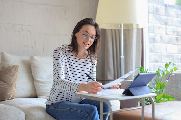 Smiling girl sit on couch watching webinar on laptop Happy young woman study on online distant course