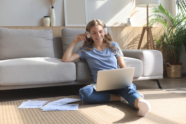 Smiling girl sit near couch watching webinar on laptop. Happy young woman study on online distant course.