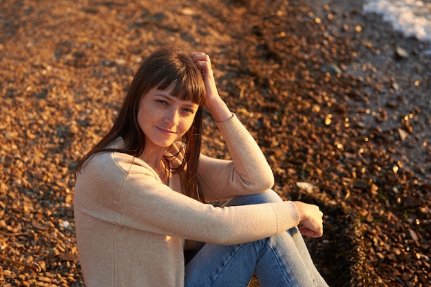 Smiling girl sitting on the beach at sunset