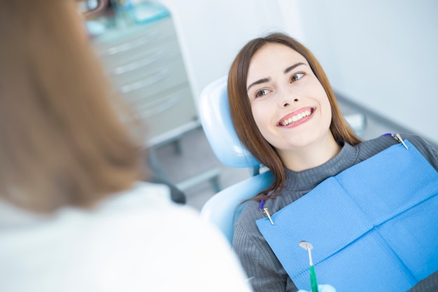 Улыбающаяся девушка, сидящая в стоматологическом кресле, осматривается врачом.