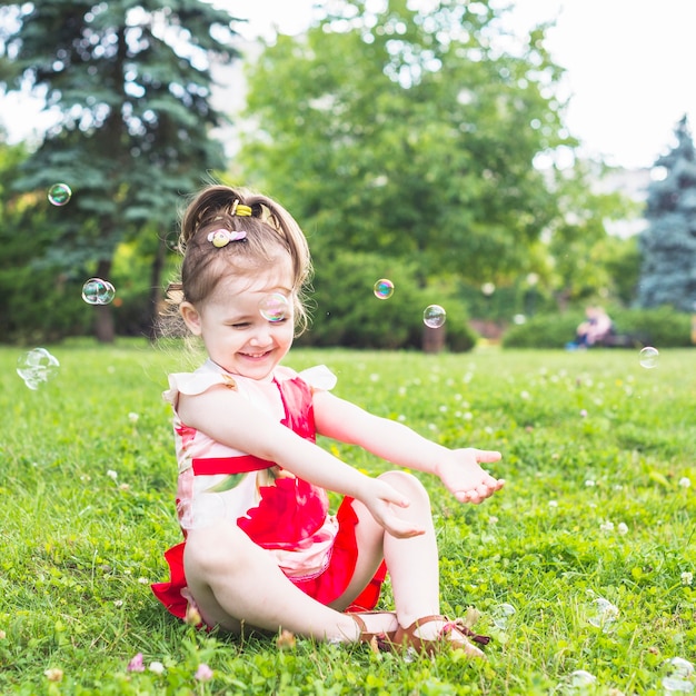 写真 透明な泡で遊んでいる緑の草に座っている笑顔の少女