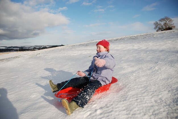 Photo smiling girl sledging on snow against sky
