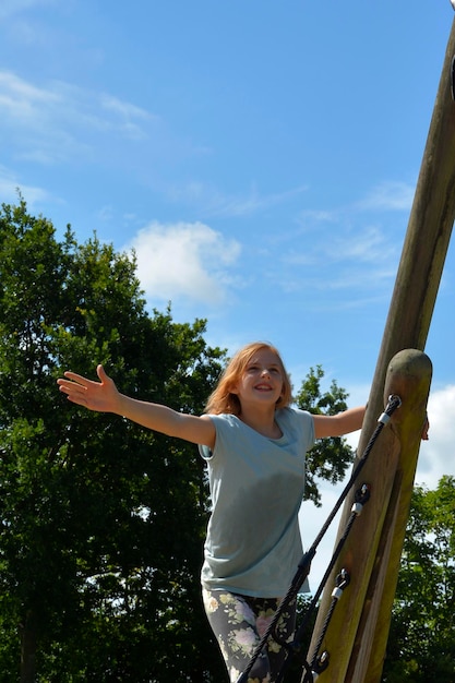 Foto ragazza sorridente in piedi sull'attrezzatura contro gli alberi e il cielo