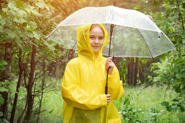 笑顔の女の子が傘を持って雨の森に立っています。