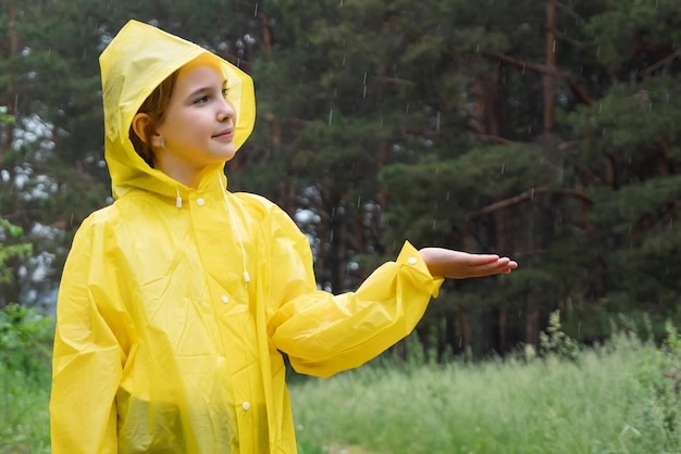 Smiling girl stands in rainy forest catching raindrops