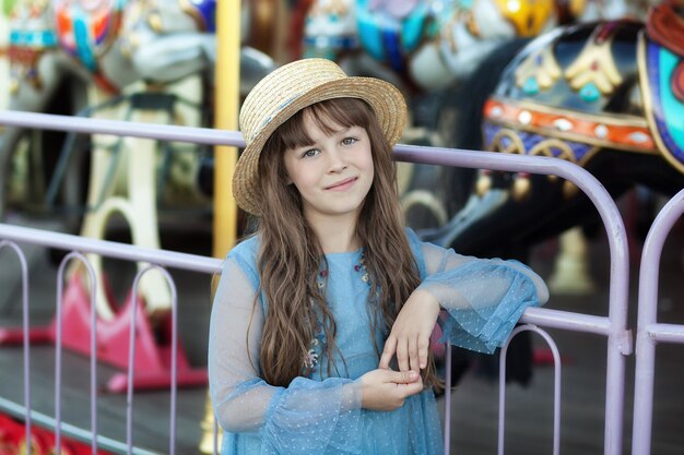 smiling girl in straw hat near carousel at fair Portrait cute girl on amusement park