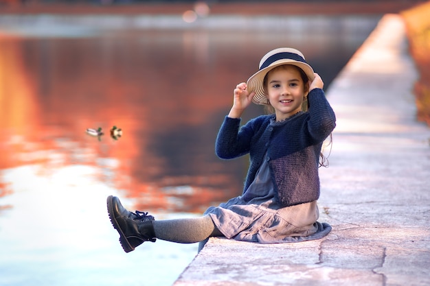 Smiling girl in straw hat sitting near pond