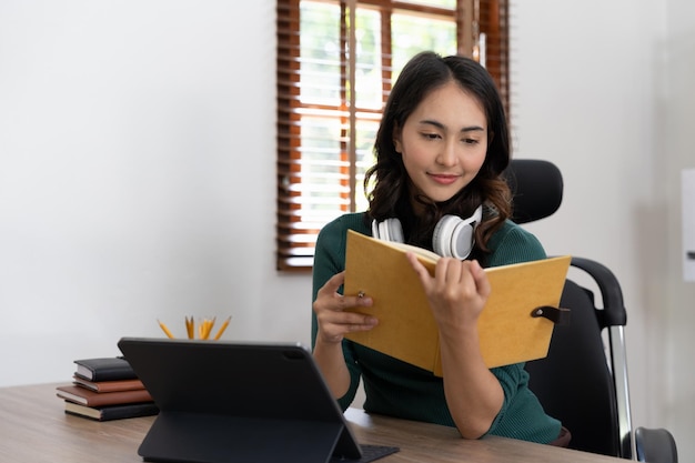 笑顔の女子学生は、ラップトップ コンピューターを使用してヘッドフォンをオンラインで勉強します。幸せな若い女性は、言語を学び、講義を視聴し、ウェビナーを書き、メモを書きます。