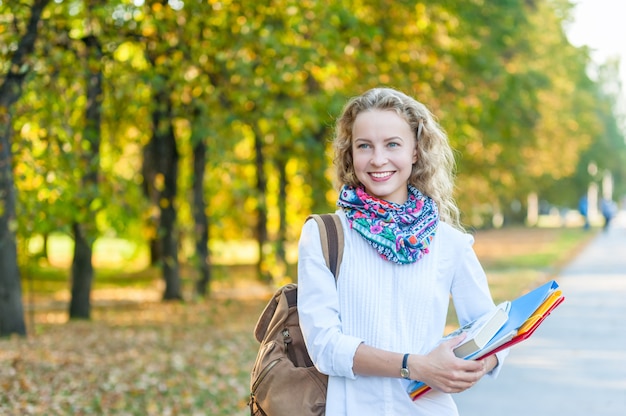 Smiling girl student with folders and books walking in the autum