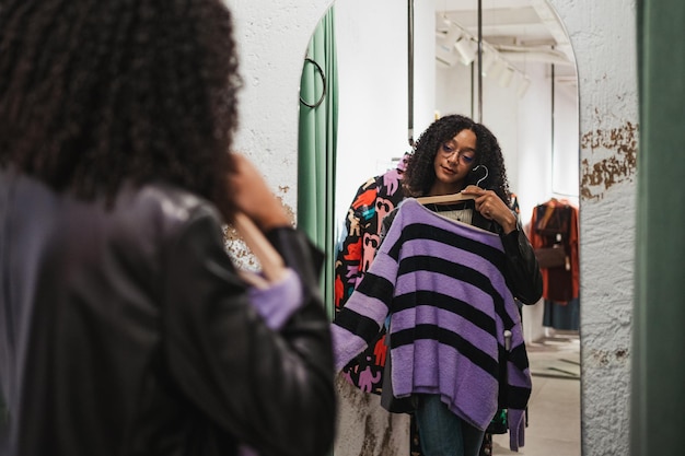 Smiling girl trying on a sweater in a fitting room she is\
looking at herself in the mirror