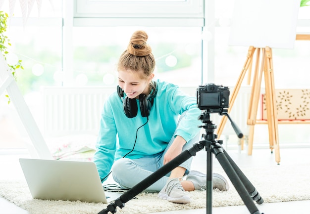Smiling girl using laptop and dslr camera in bright room