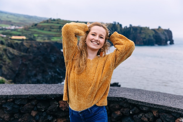 暖かいセーターを着た笑顔の女の子が山の緑の湖を背景に立っている幸せな女性が旅をしている